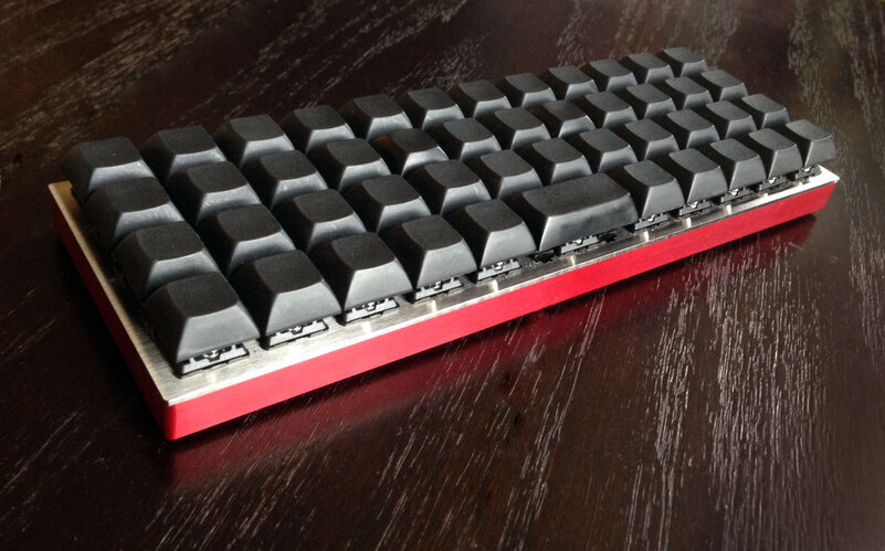 Photograph of a Planck keyboard with steel plate, red milled bottom, and blank black DSA-profile key caps
